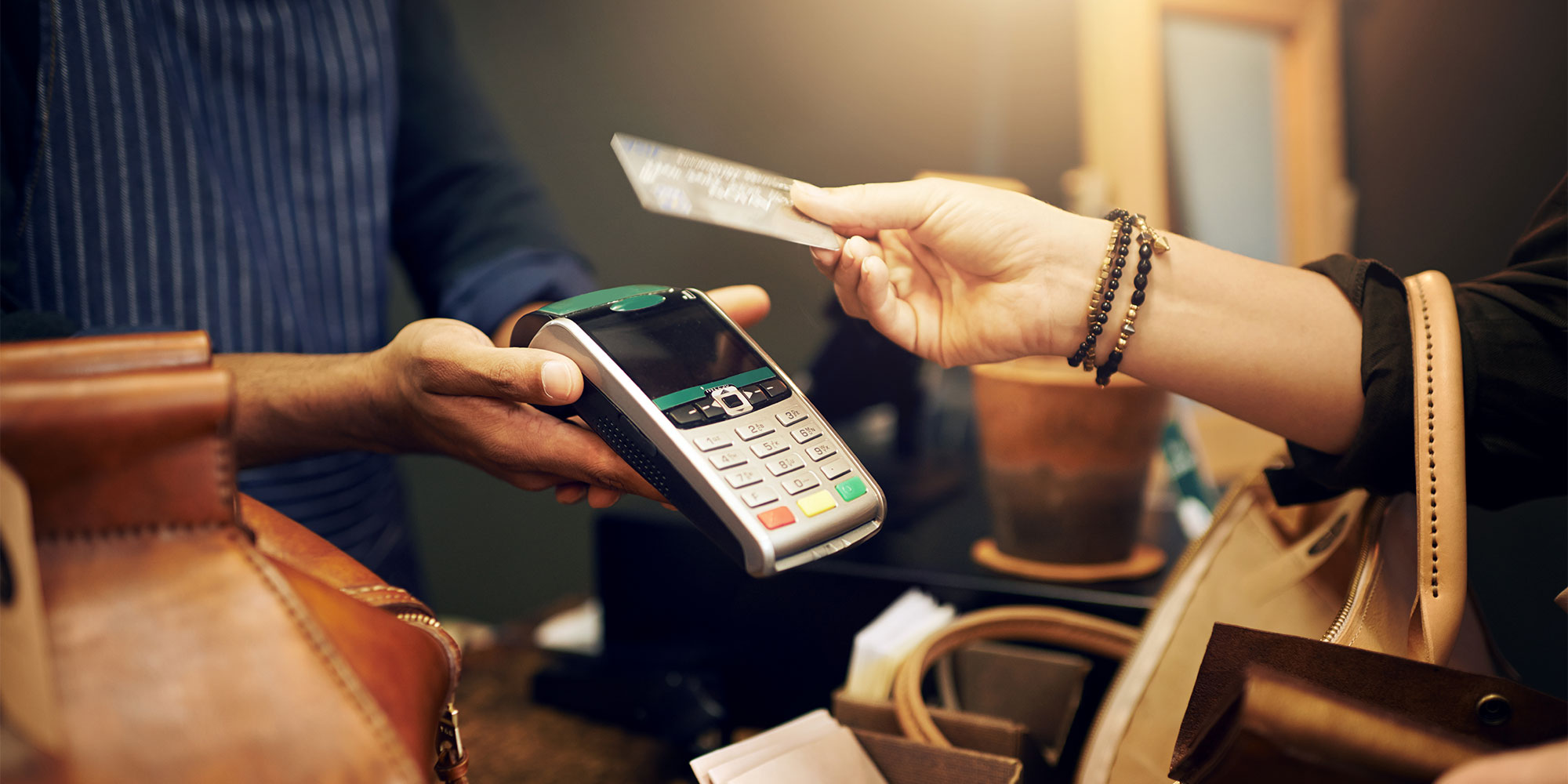 A hand containing a bank card is poised above a card reader, ready to tap.