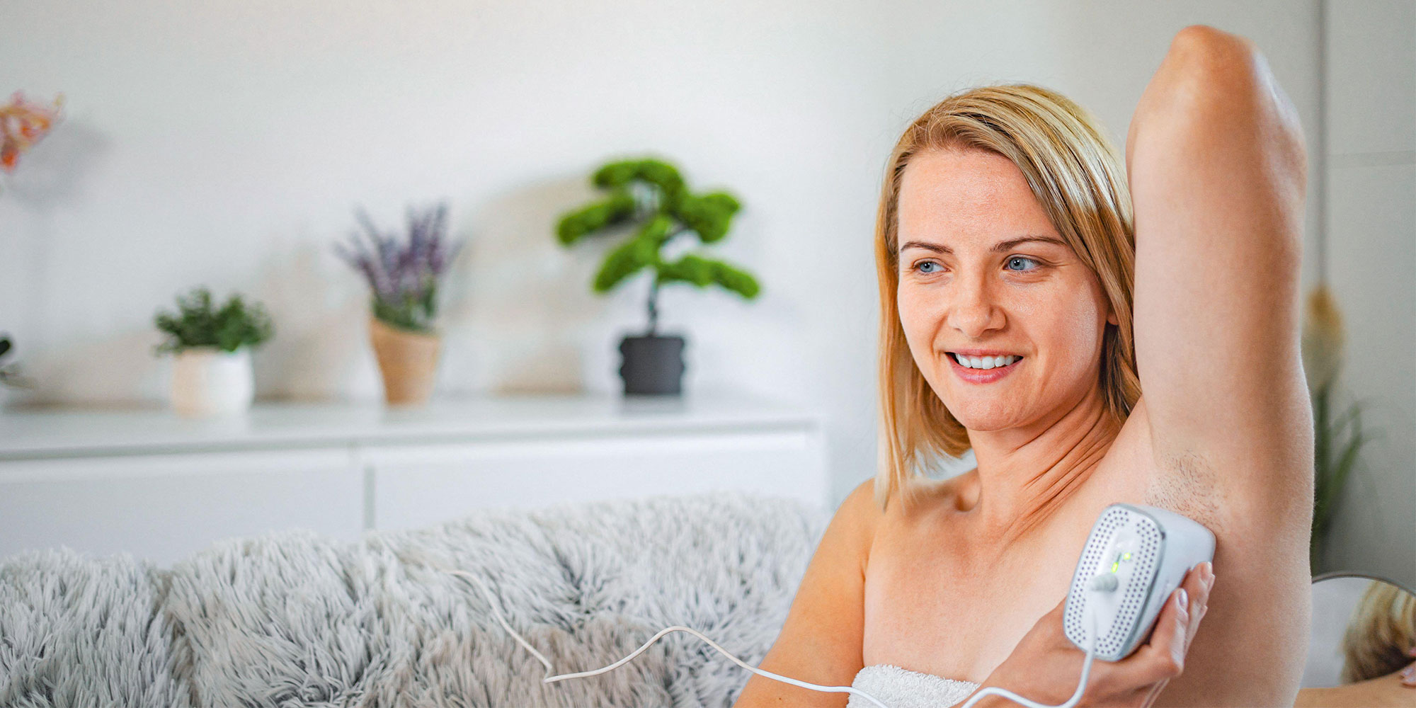 Woman in a white towel using a white IPL hair removal device on her armpit.