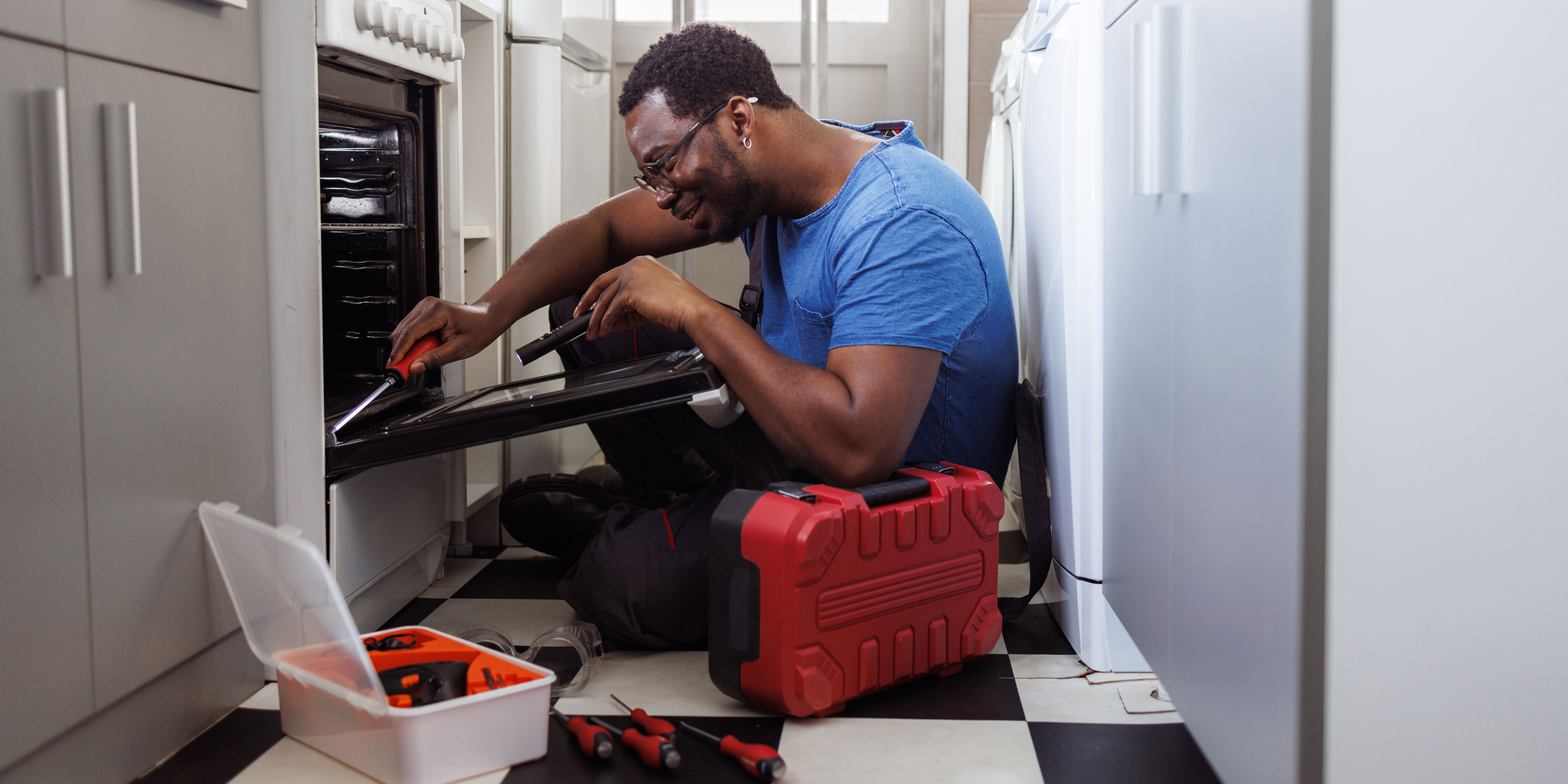 man repairing a freestanding oven in a narrow kitchen