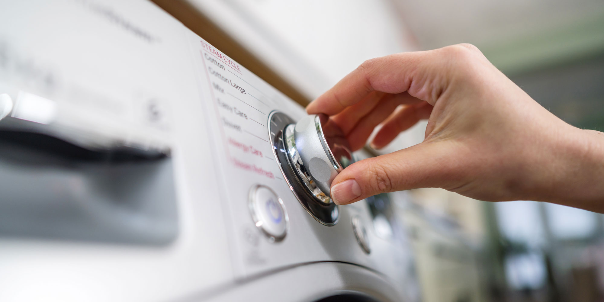 A hand turning a washing machine dial