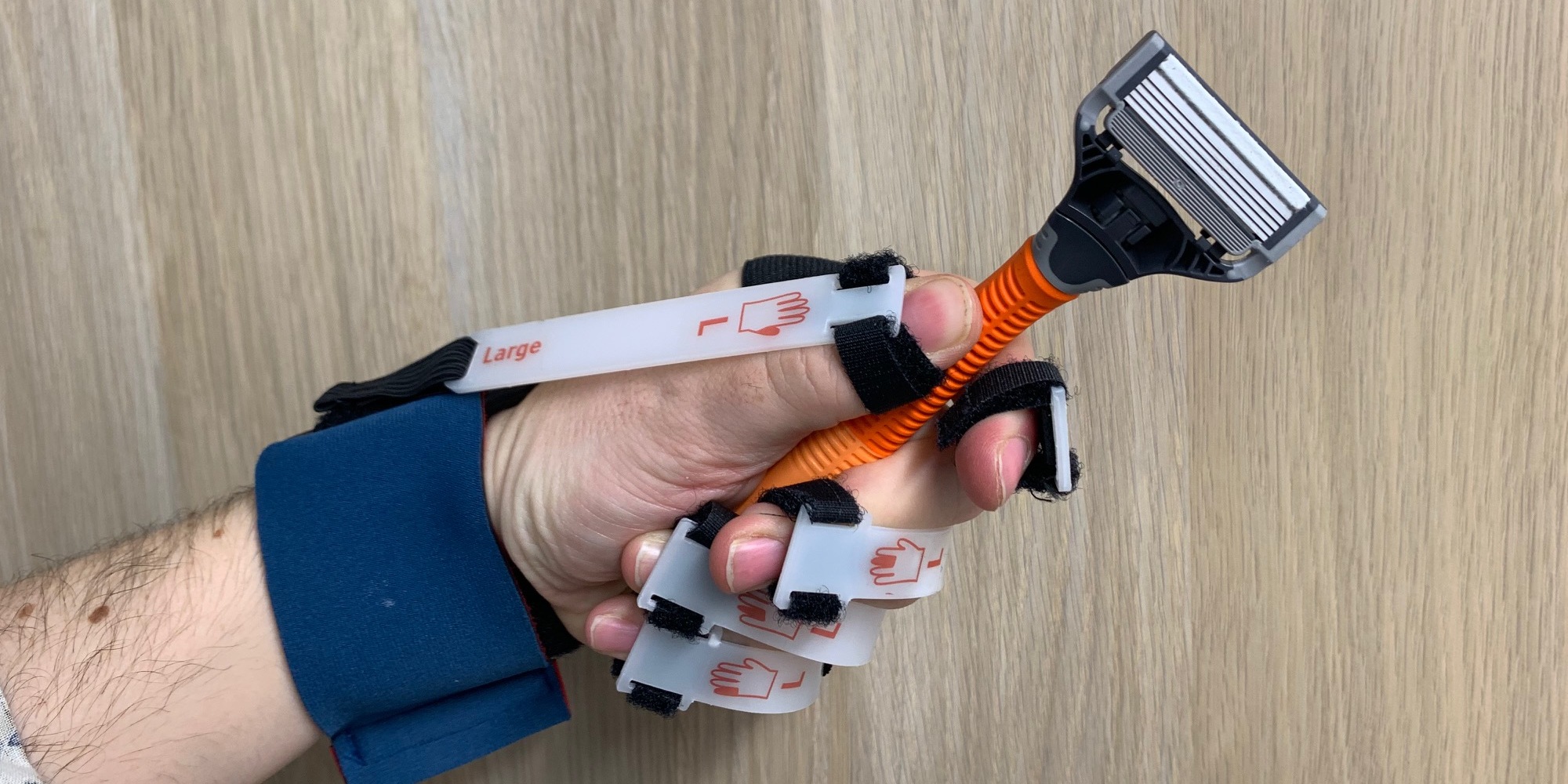 Orange razor being held in Cambridge simulation glove for reduced hand strength