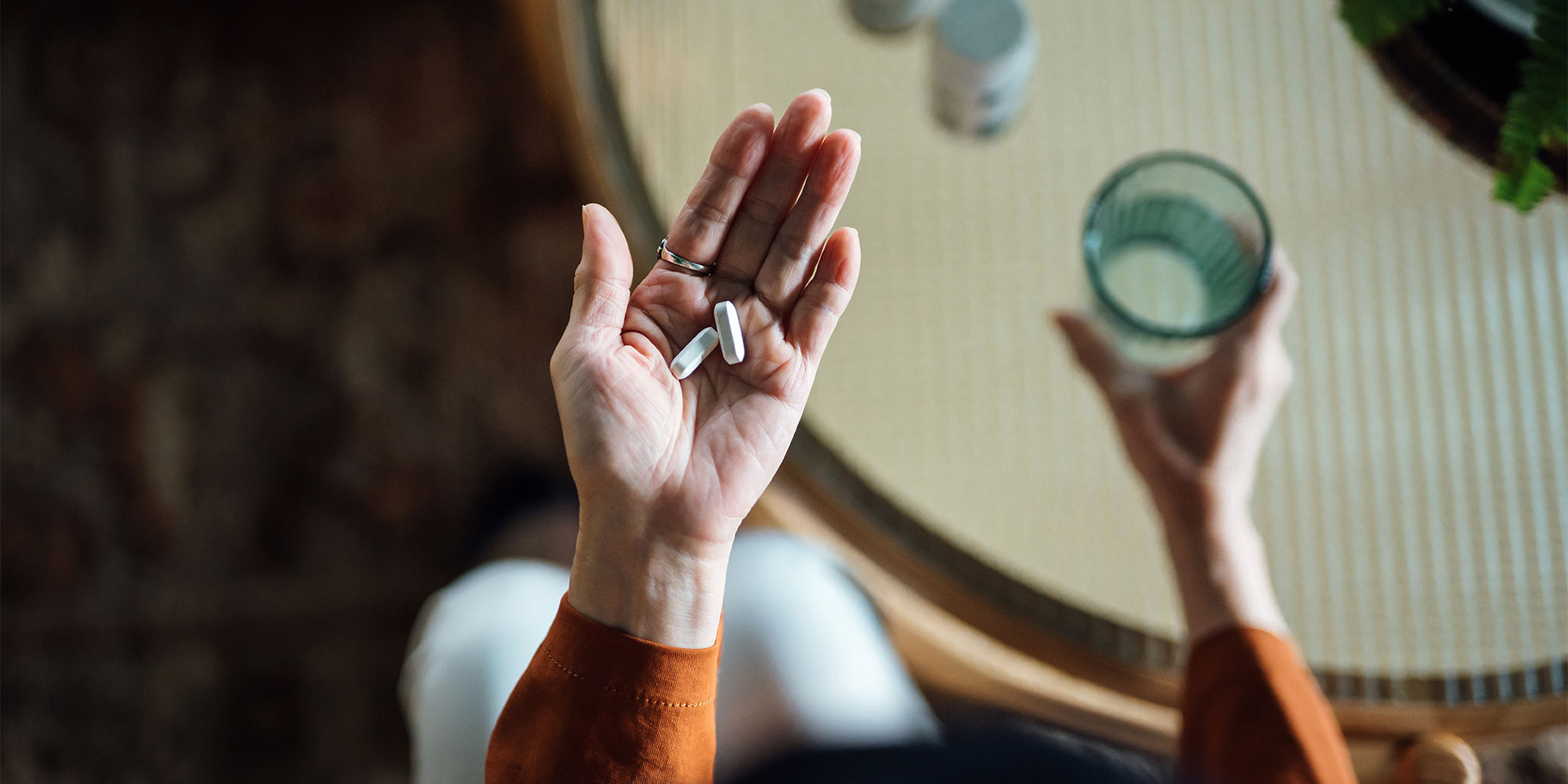 Two tablets in the hands of someone about to take them with a glass of water