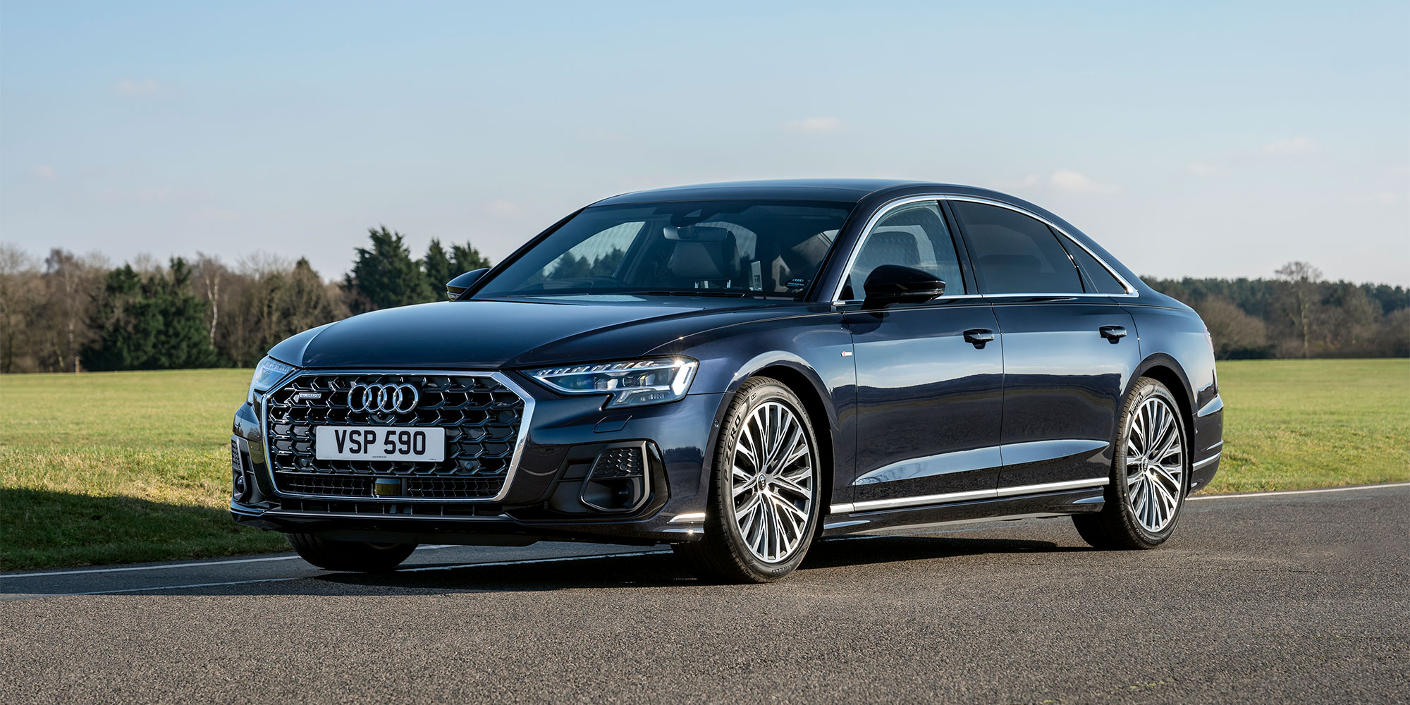 Dark blue Audi A8 L with number plate VSP 590 on a road with green fields and trees in the background.