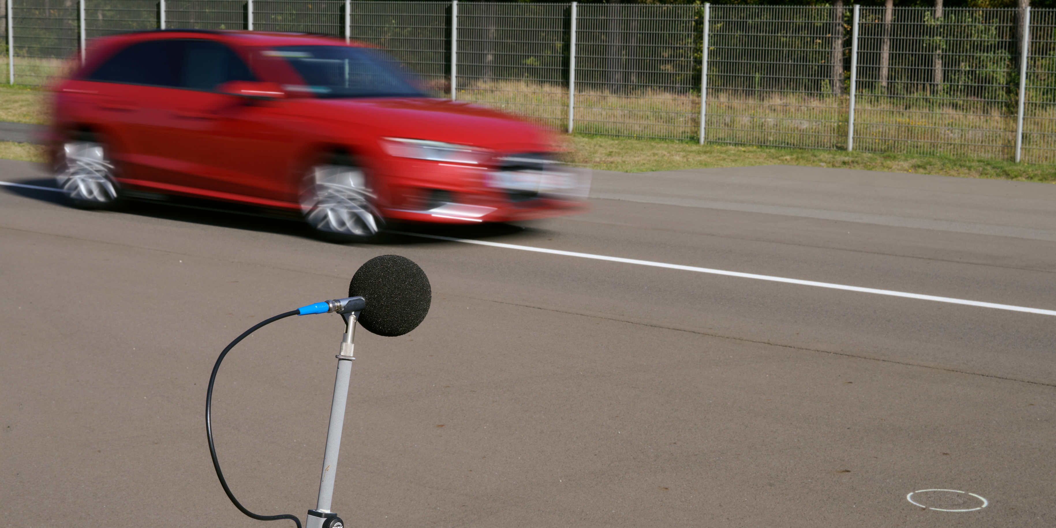 Microphone testing tyre noise of red car on road