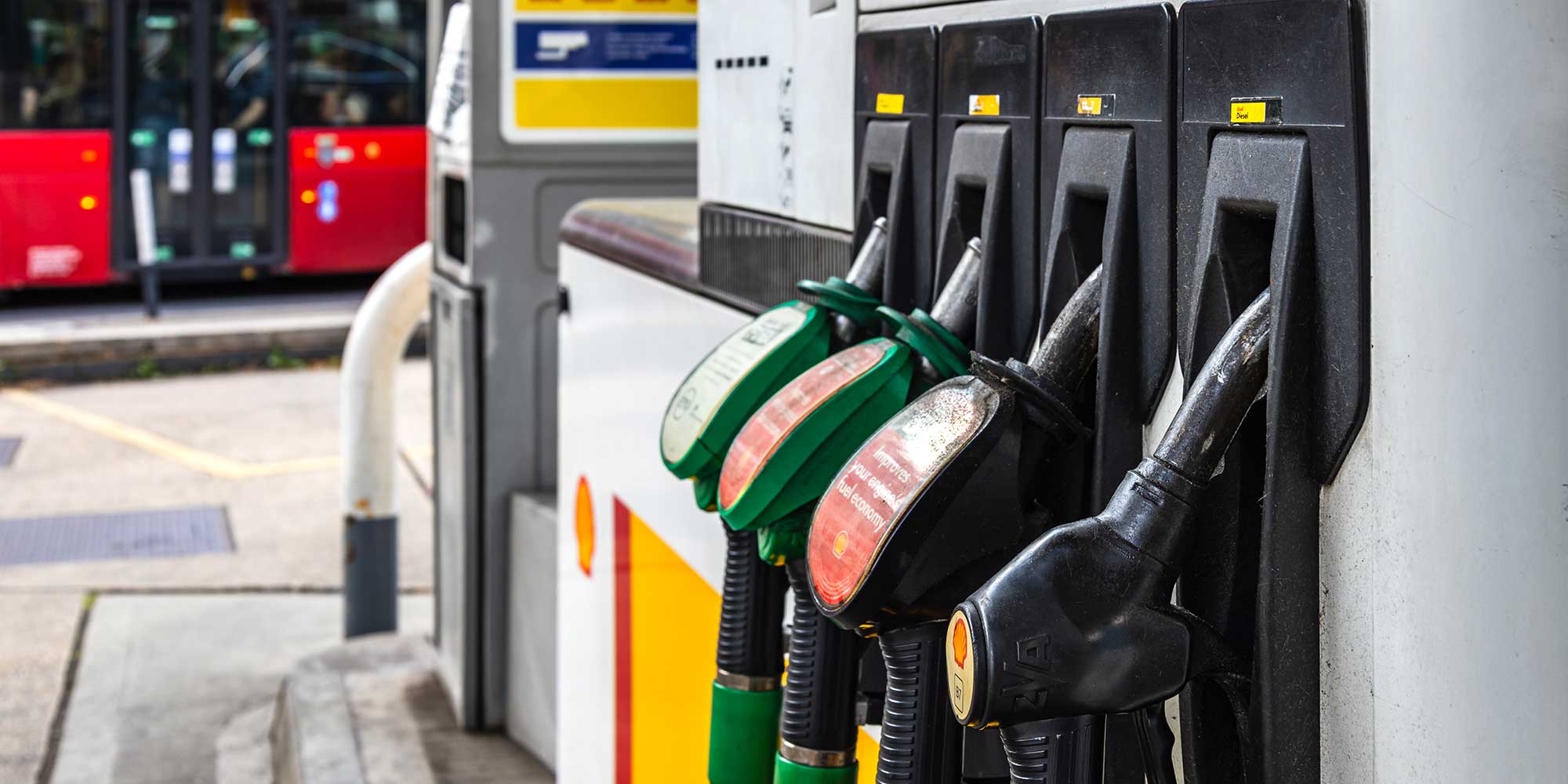 A petrol pump at a Shell filling station in the UK, with a red bus in the background.