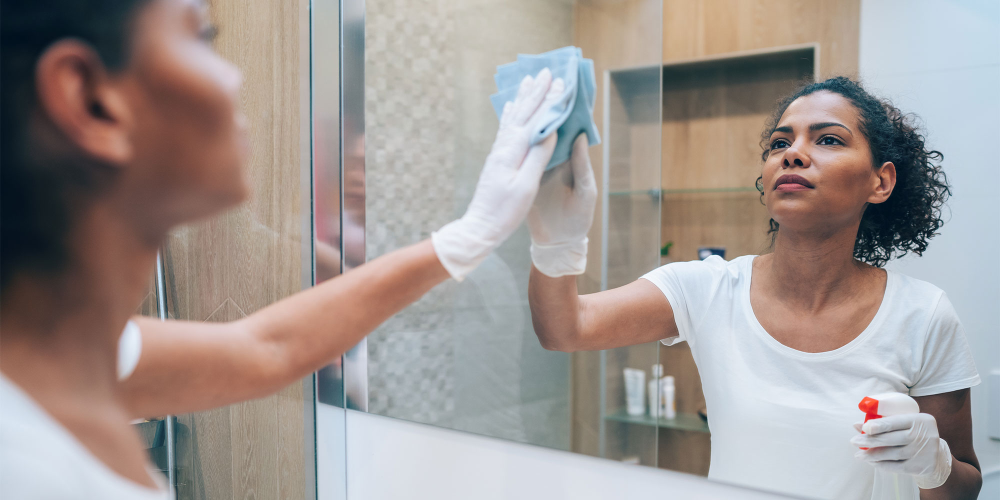 A person cleaning a mirror with a cloth and spray