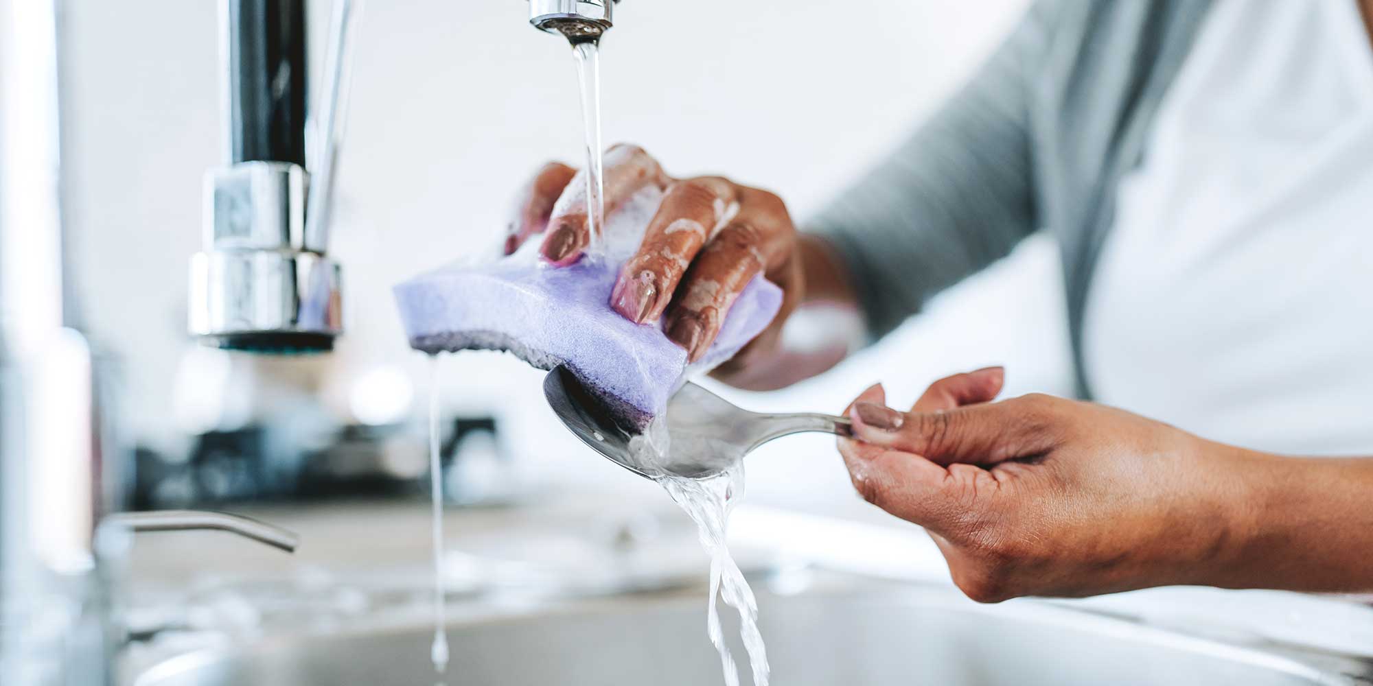A person cleaning a spoon with a sponge