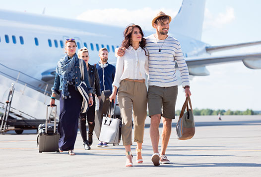Group of travellers with luggage walking away from an airplane on a sunny day.