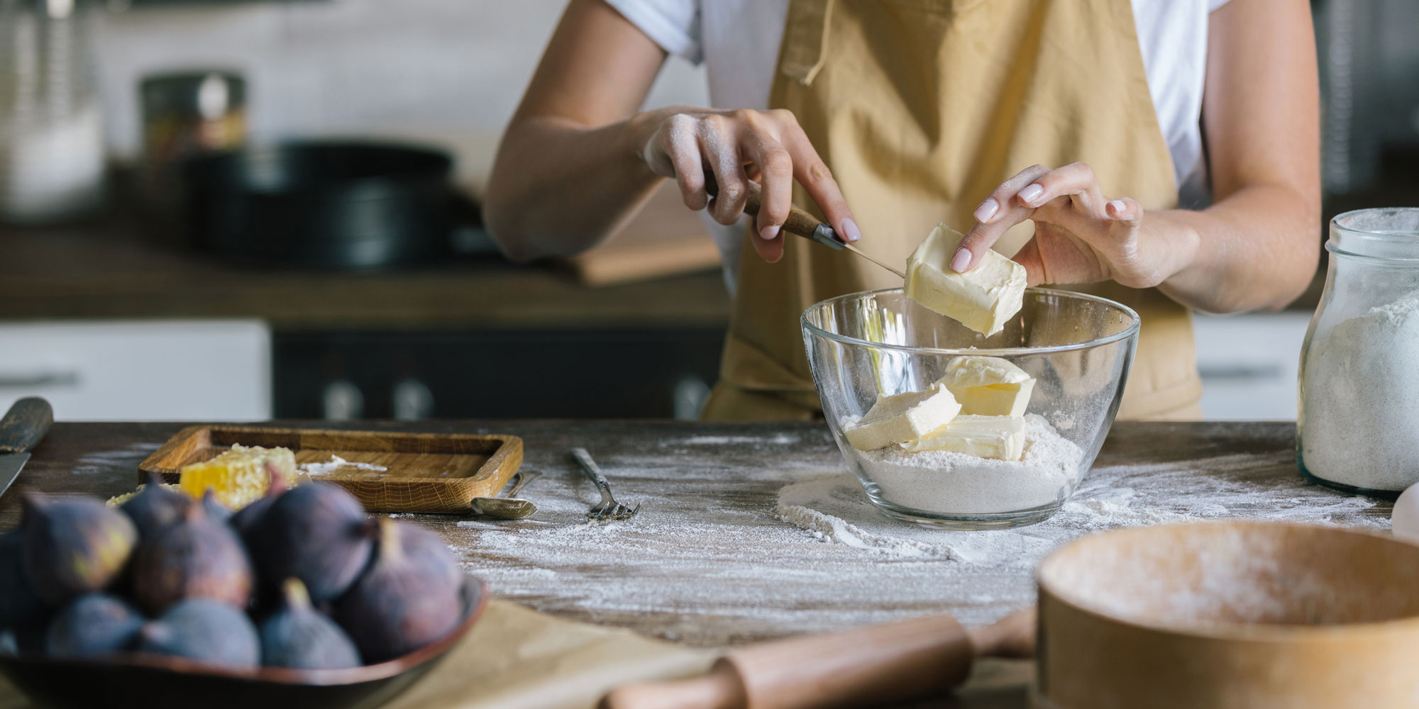 Someone baking and cutting a block butter or similar into a glass mixing bowl with flour in it.