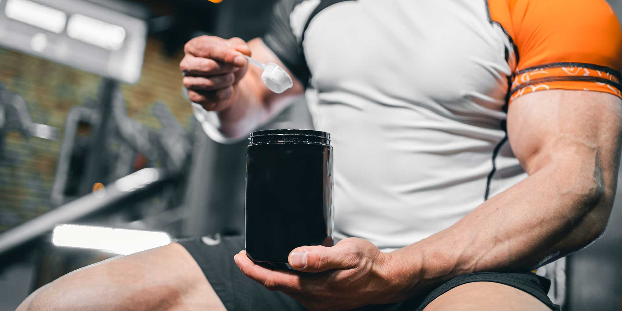 Muscular man taking a spoonful of creatine powder at the gym