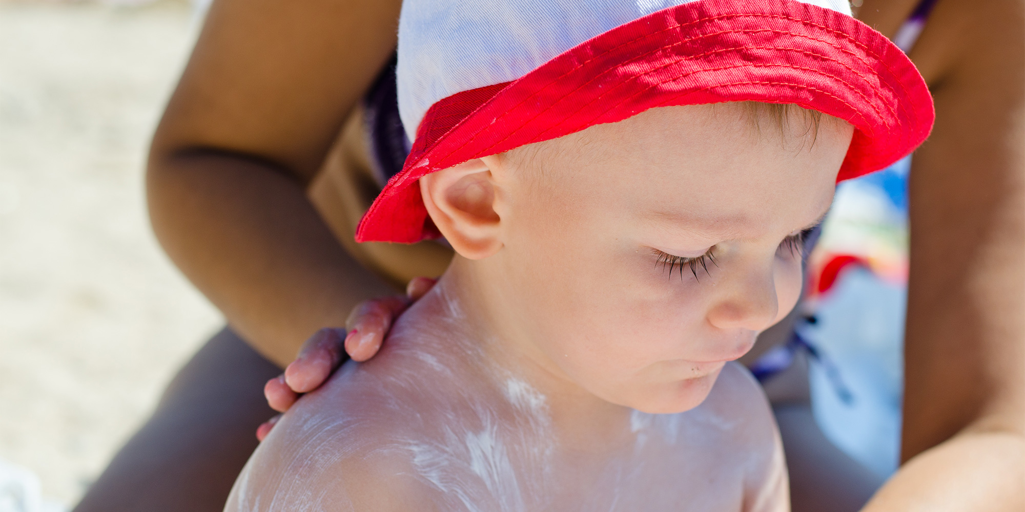 mum at the beach applying sunscreen on a baby