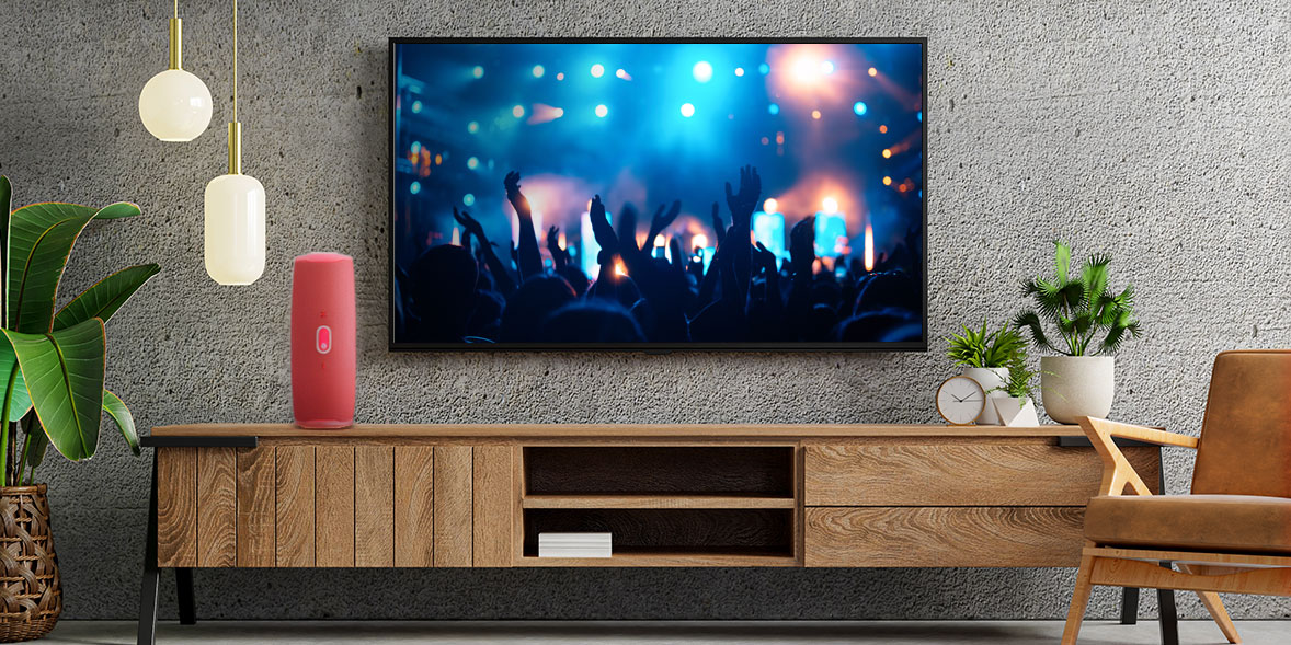 A Bluetooth speaker is on a TV cabinet next to a TV