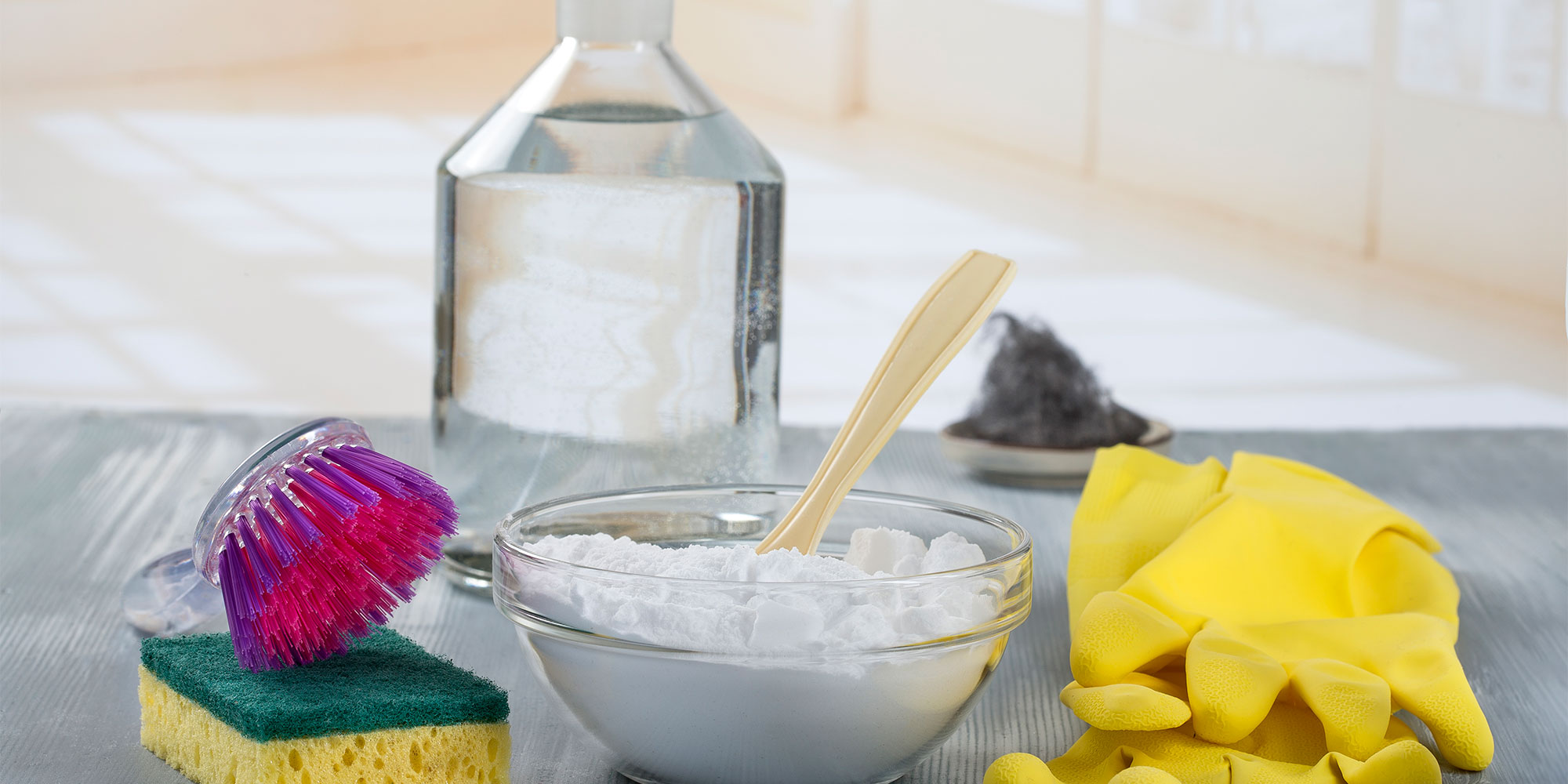 a bowl of bicarbonate of soda, bottle of white vinegar, cleaning brush, sponge and gloves