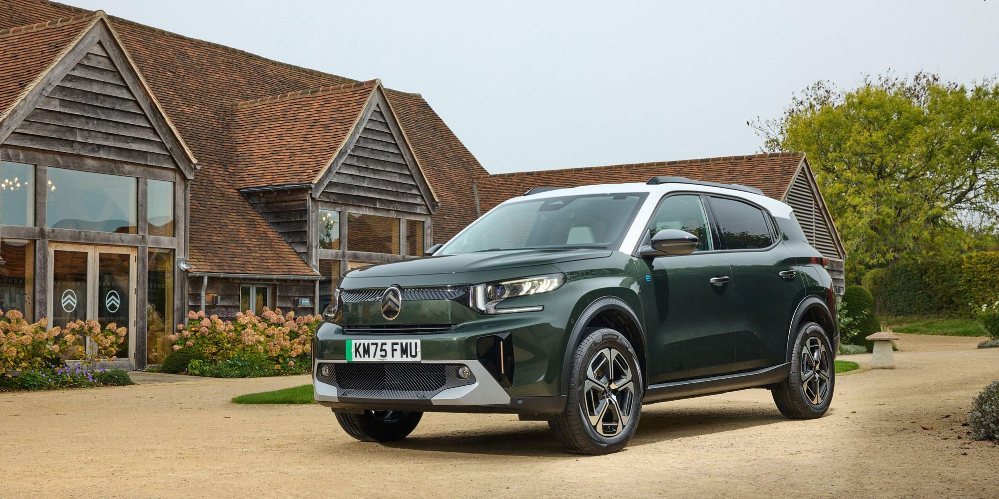A green and white Citroen e-C3 Aircross parked in front of a wooden building