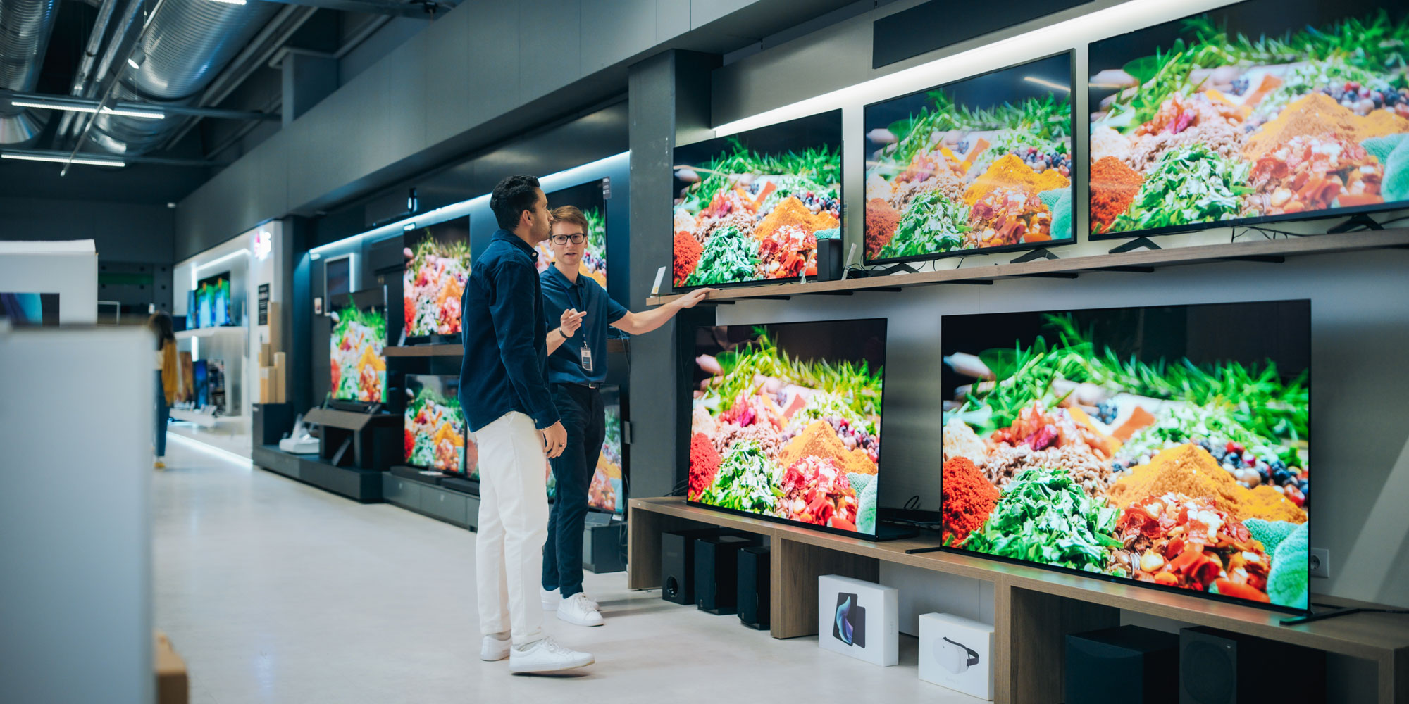 A man is talking to a sales assistant while shopping for a TV 