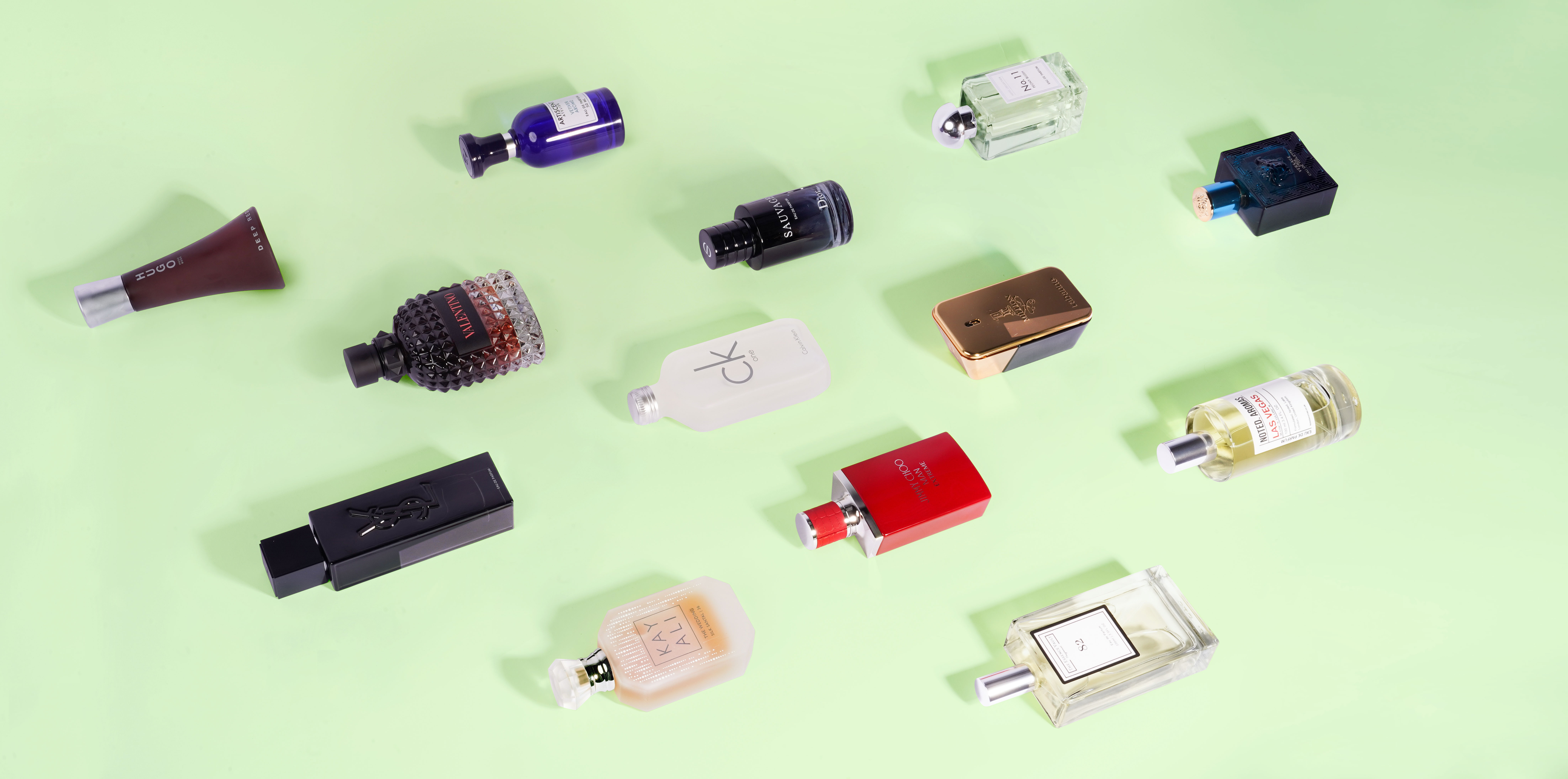 12 perfumes for men lying on their side against a green background