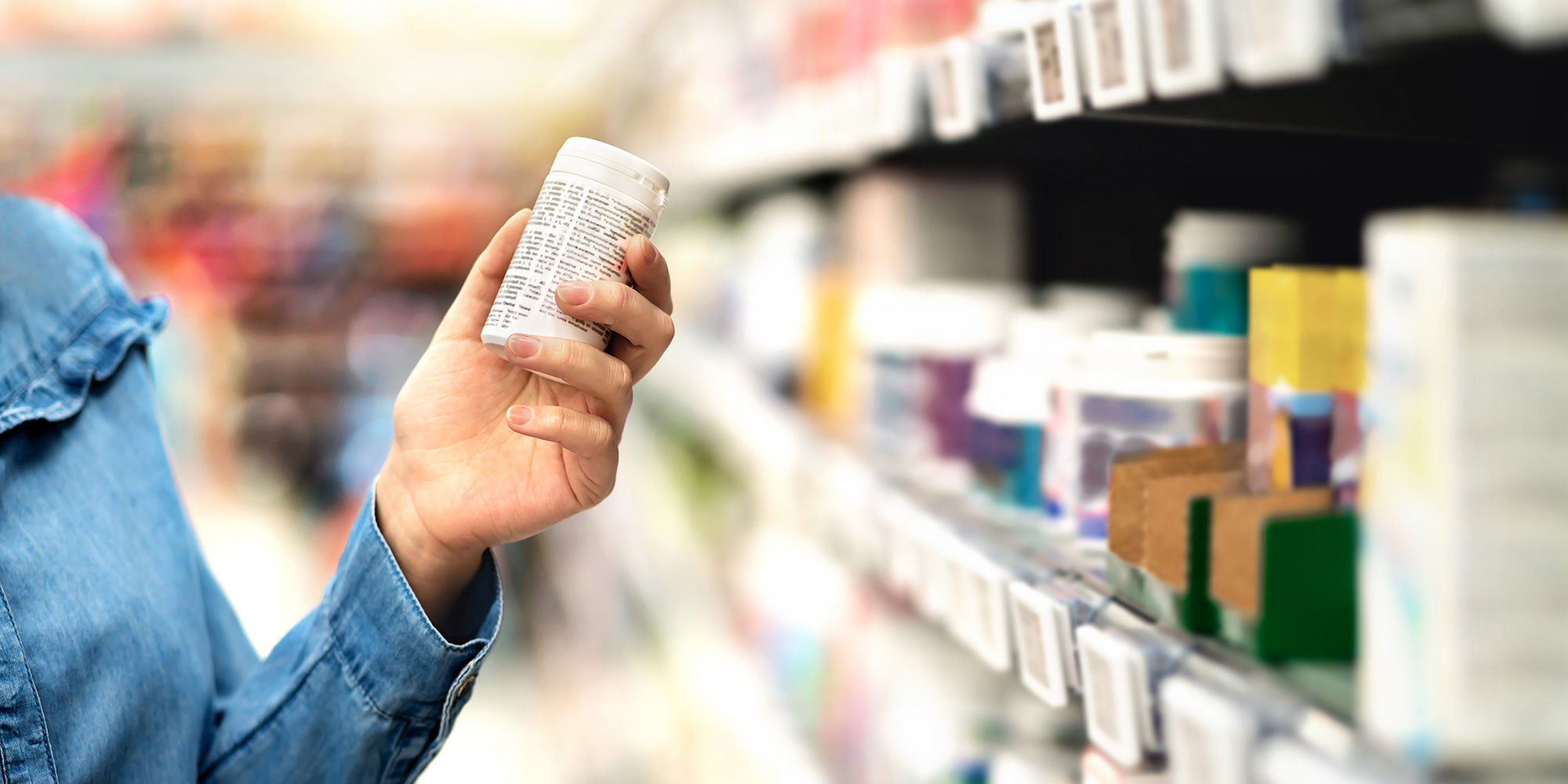Hand reaching for a packet of pills or supplements on a shelf in store