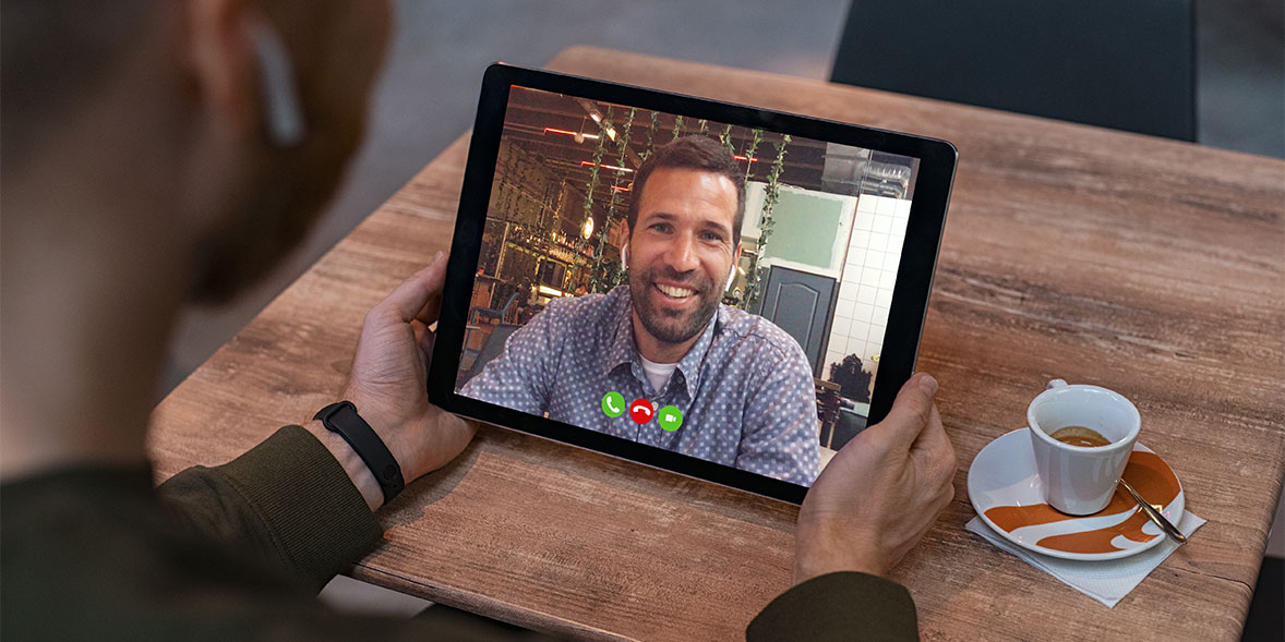 A man in a coffee shop making a view call on his tablet