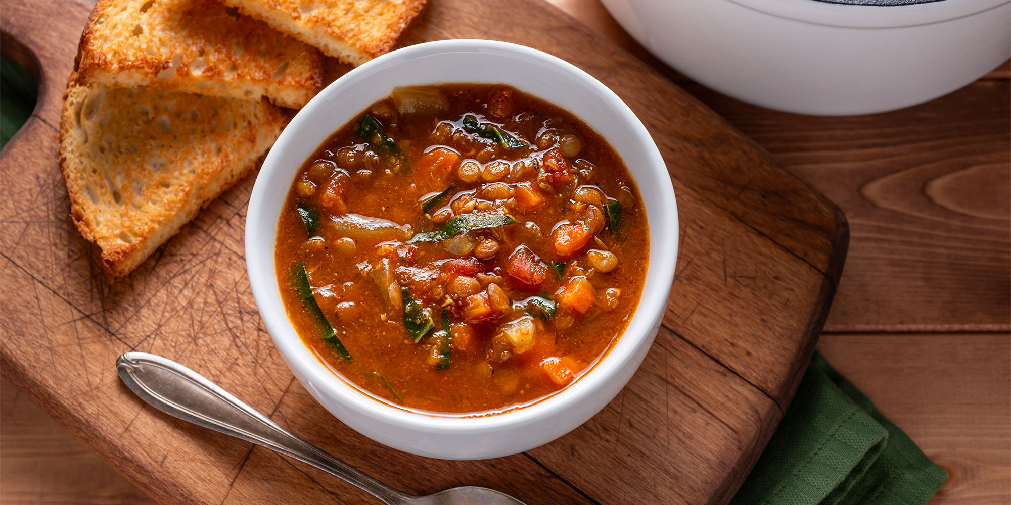 A bowl of vegetable soup, with a few slices of toast next to it.