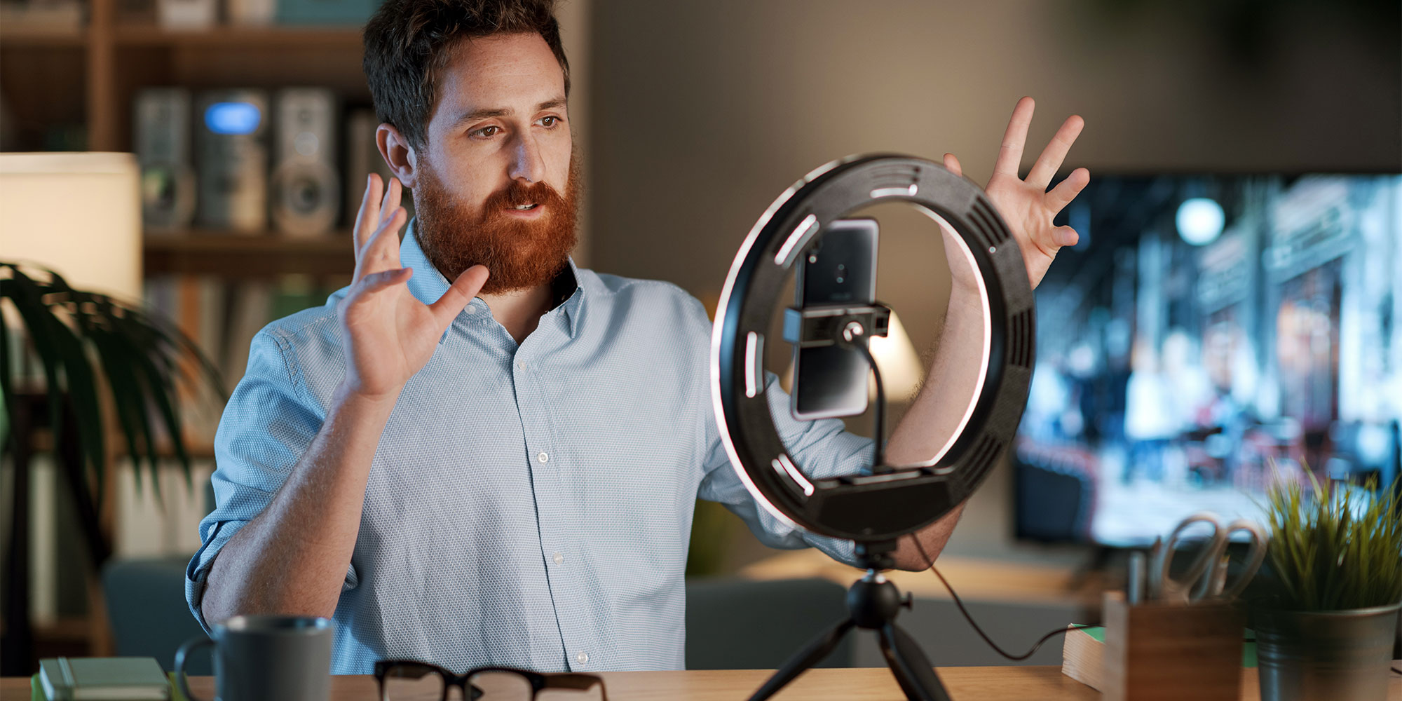 Man with beard in blue shirt using a ring light to record video content.