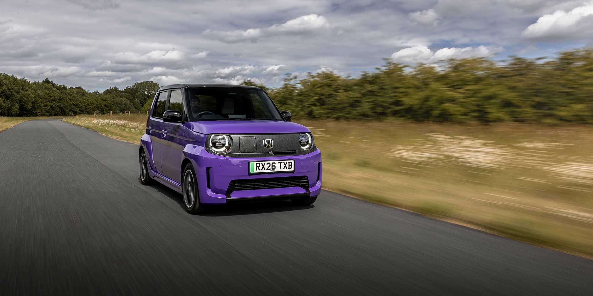Purple Honda Super-N drives down road lined with trees and grass.