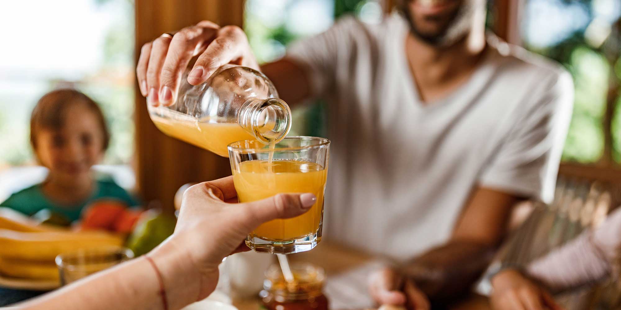 Someone pouring an orange juice into a waiting glass