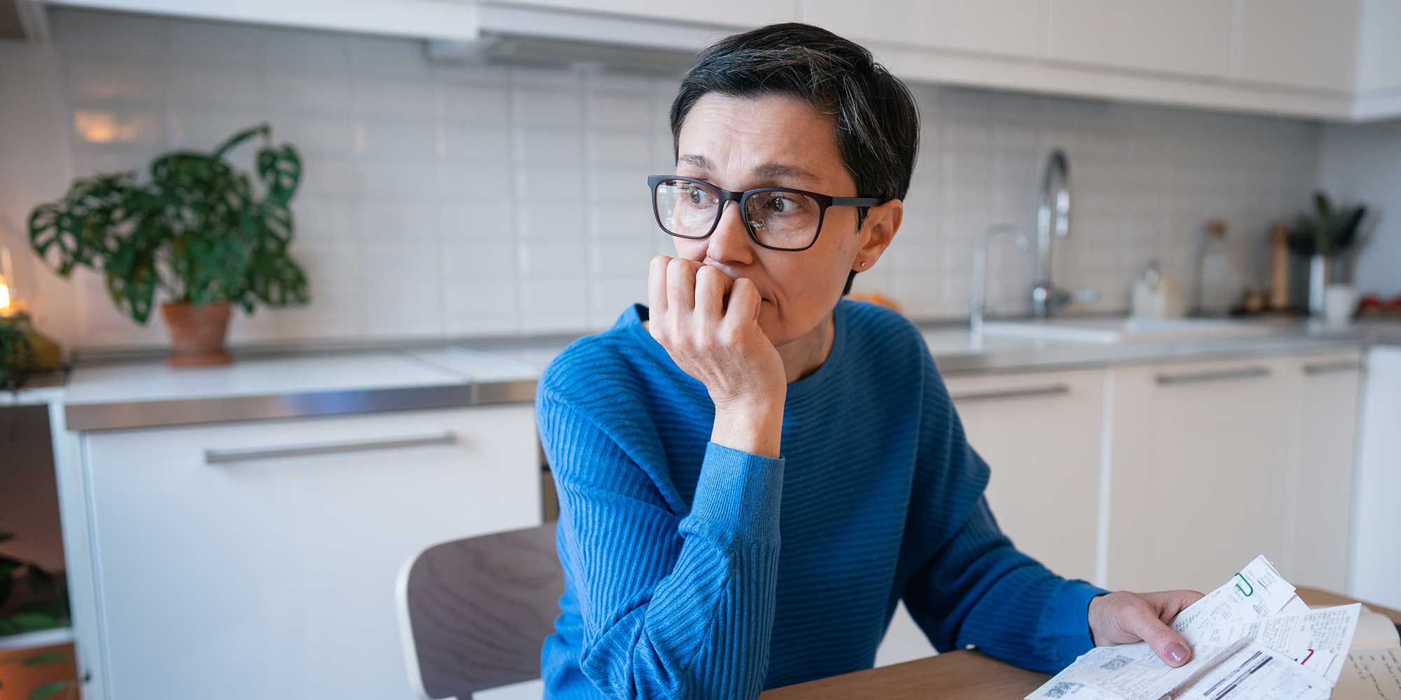 Woman sitting at a kitchen table holding an energy bill looking worried