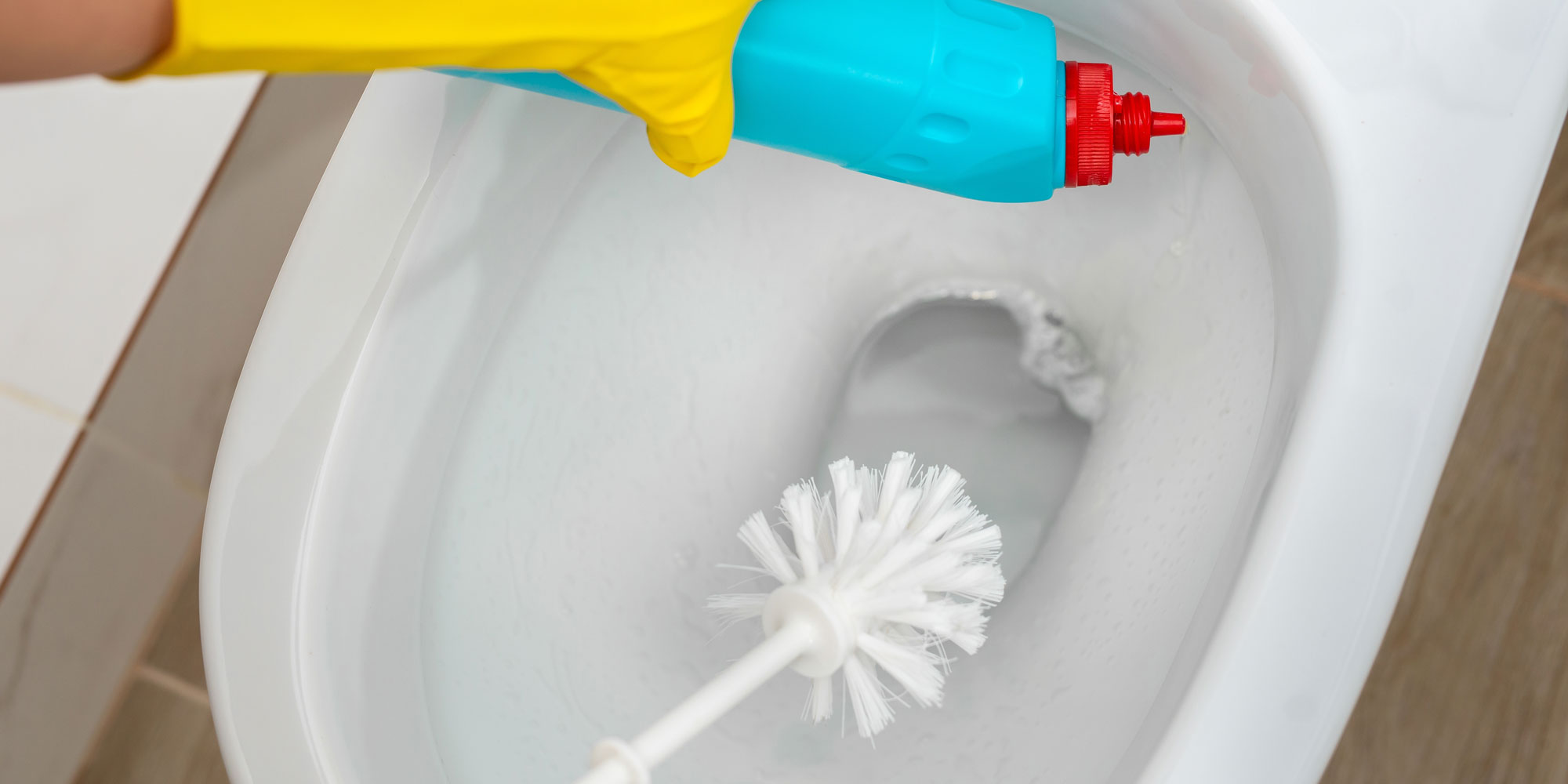 person cleaning a toilet bowl with bleach and a toilet brush