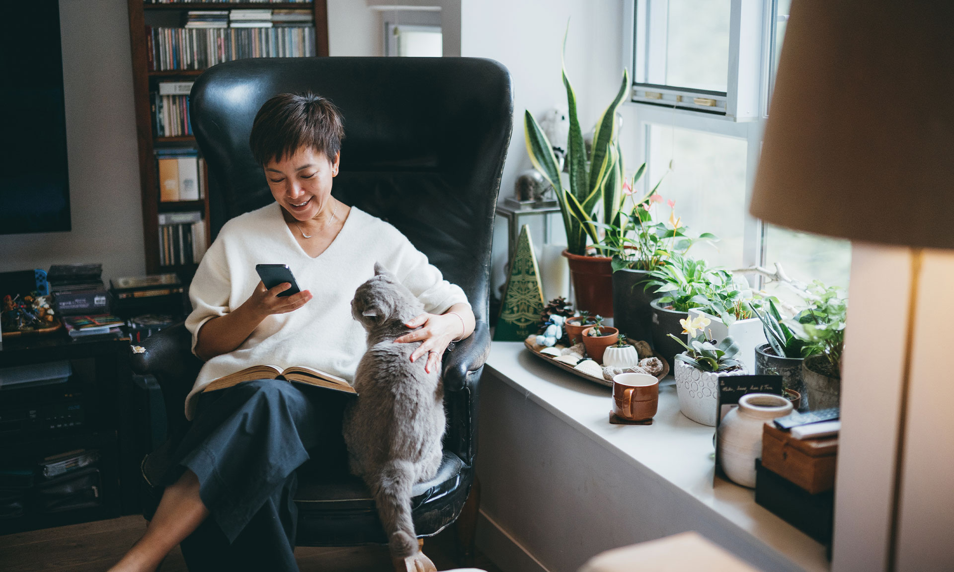 woman sitting in chair with cat, looking at mobile phone