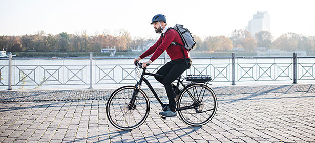 Man in red jumper riding electric bike on cobbled street next to river