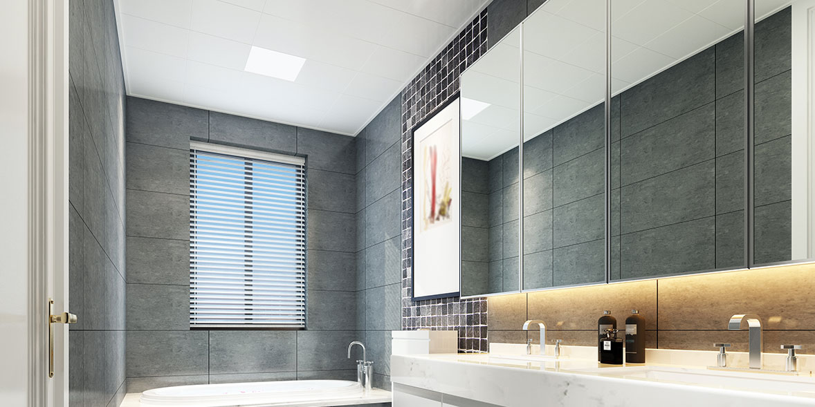 Mirrored bathroom wall cabinets above white bathroom units in a grey tiled bathroom with white bath and toilet