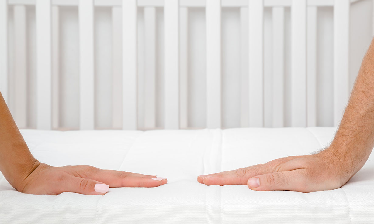two hands pressing down on white cot mattress