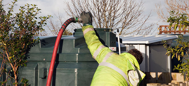 Man in high-visibility jacket and gloves using a hose to fill a heating oil tank