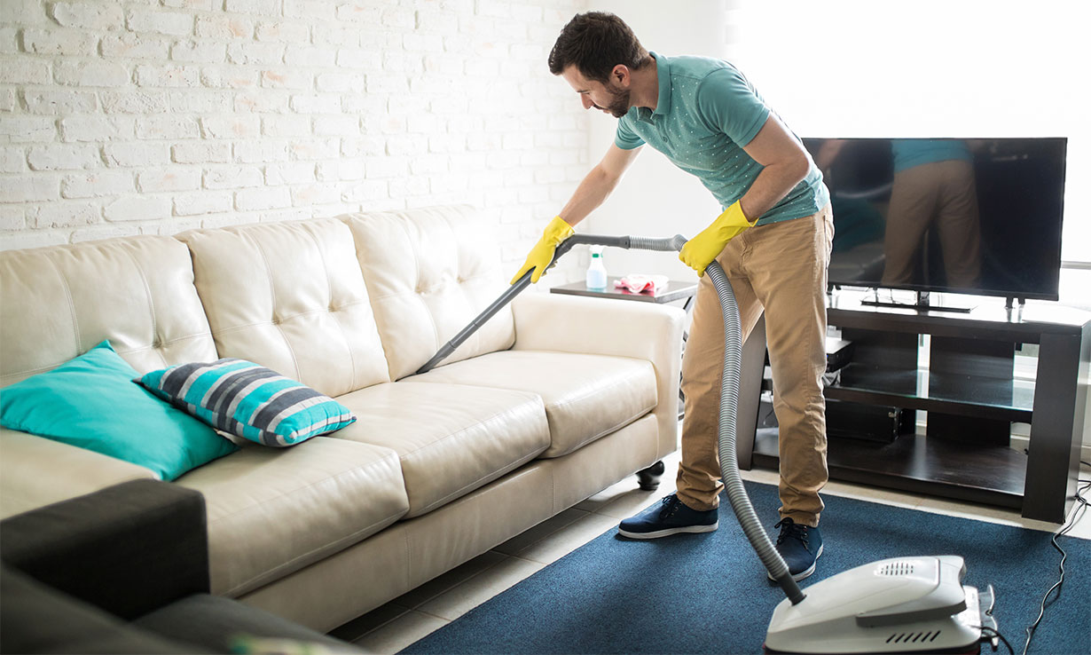 Man vacuuming a white sofa