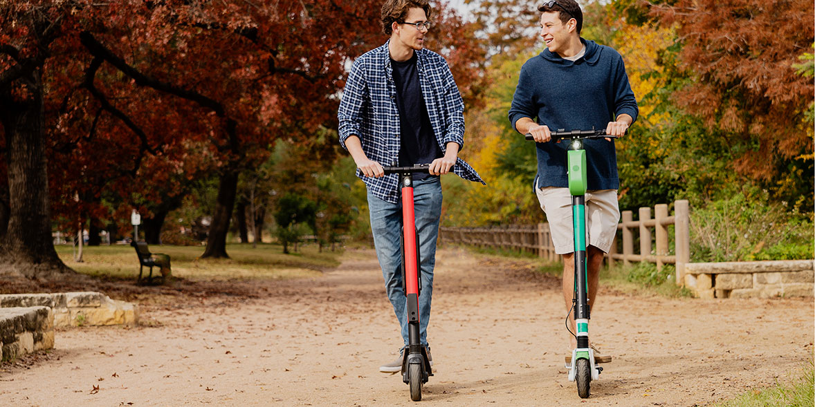 Two friends riding electric scooters in a park