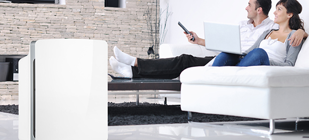 Couple sitting on a sofa with an air purifier in the corner of the room