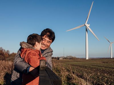 Man and child hugging by a fence in front of wind turbines generating renewable electricity.