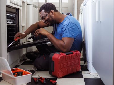 man repairing a freestanding oven in a narrow kitchen